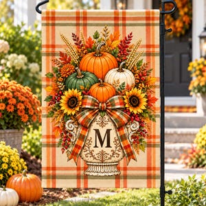 May include: A rectangular garden flag featuring a plaid background in orange, tan, and green. The centre displays a decorative urn with the letter M, overflowing with pumpkins, sunflowers, wheat stalks, and autumn leaves, tied with a plaid bow.