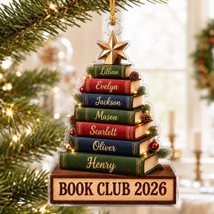 May include: A clear acrylic Christmas tree ornament shaped like a stack of books with the names Lillian, Evelyn, Jackson, Mason, Scarlett, Oliver, and Henry printed on the spines. A wooden base features the text BOOK CLUB 2026 and a gold star topper.