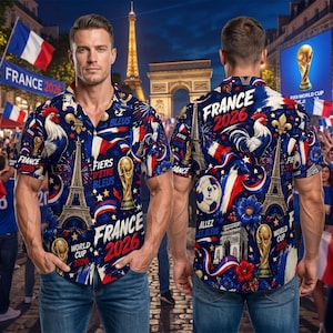 May include: A short-sleeved button-down shirt with a navy blue background, featuring a design of the Eiffel Tower, a soccer ball, and the text "France 2026". The shirt's design incorporates the colors red, white, and blue.