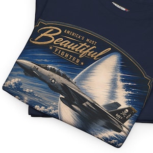 May include: Navy blue t-shirts with a graphic of a fighter jet. The graphic reads "America's Most Beautiful Fighter" in a vintage style. The jet is depicted in flight against a blue sky.