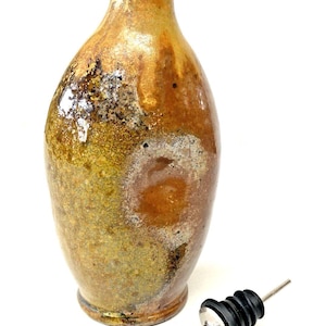 May include: A handcrafted, glazed ceramic bottle with a brown and gold mottled finish. A stainless steel pour spout with a black rubber stopper sits beside the bottle. The bottle has a narrow neck and a rounded body.