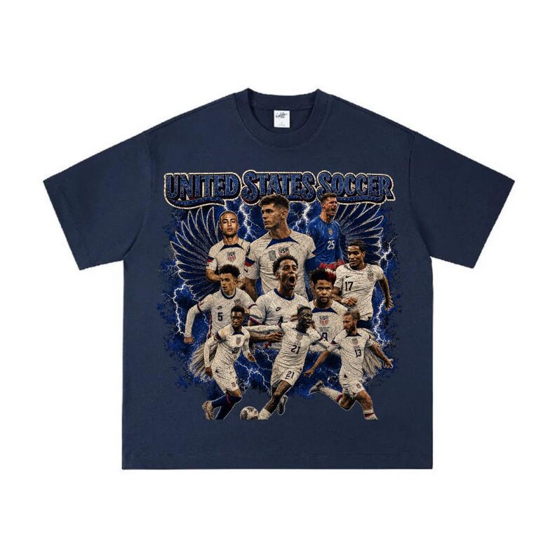 May include: A navy blue short-sleeve t-shirt featuring a graphic print of the United States soccer team. The design includes multiple players in white jerseys, blue lightning bolts, and wings, with the text UNITED STATES SOCCER at the top.