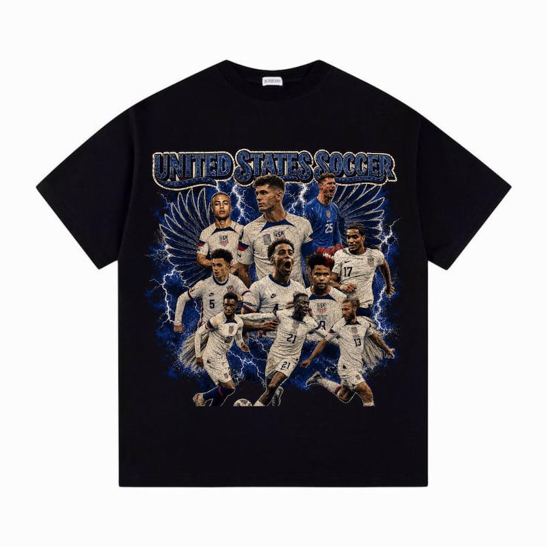 May include: A black short-sleeve t-shirt featuring a graphic print with the text UNITED STATES SOCCER. The design displays multiple soccer players in white jerseys against a background of blue lightning bolts and stylized wings.