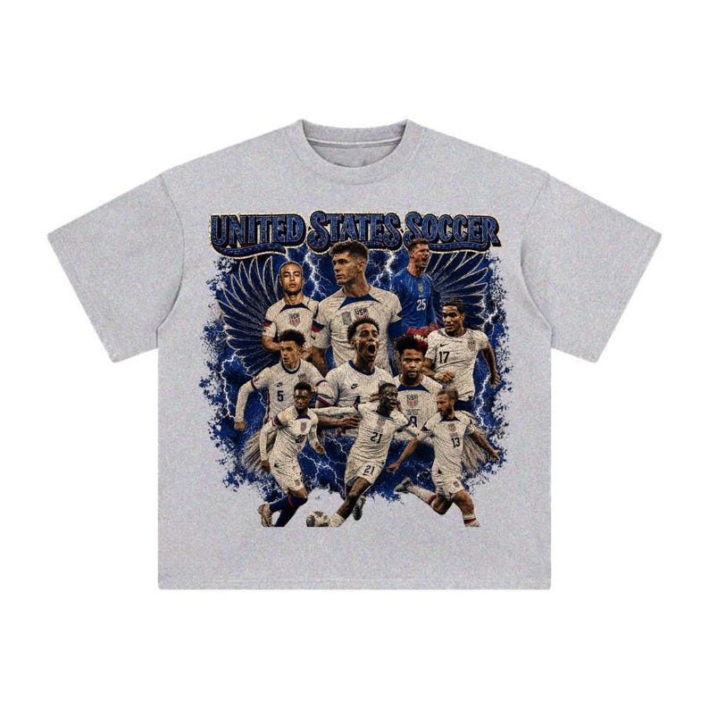 May include: A heather gray short-sleeve t-shirt featuring a graphic print of the United States Soccer team. The design includes multiple players in white jerseys, blue lightning bolts, and wings, with the text UNITED STATES SOCCER at the top.