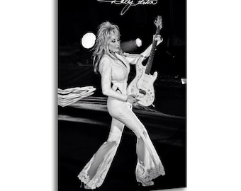 May include: A black and white canvas print featuring Dolly Parton playing an electric guitar. She is wearing a long-sleeved white jumpsuit with flared lace-trimmed legs. The signature Dolly Parton is written in white script at the top of the image.