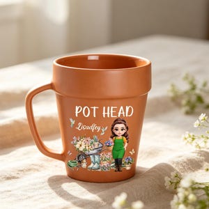 Pode incluir: Uma caneca de cerâmica cor de terracota em forma de vaso de flores com uma pega. A frente apresenta o texto POT HEAD e Lisadfey sobre um gráfico de uma pessoa com um avental verde rodeada de ferramentas de jardinagem e flores em vasos.