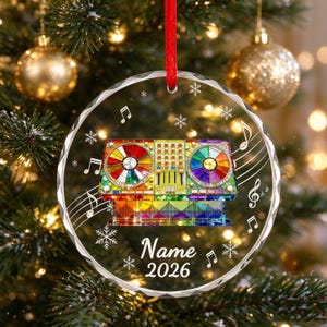 May include: A circular clear acrylic ornament featuring a colorful DJ mixing console graphic with rainbow-hued turntables. The design includes white musical notes and snowflakes, with the customizable text Name and the year 2026 printed in white.