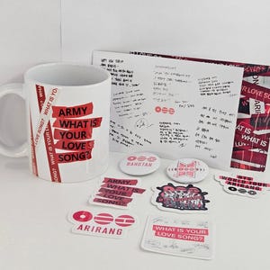 May include: A white ceramic mug with the text "ARMY WHAT IS YOUR LOVE SONG?" in red. The image also includes stickers, a handwritten note, and pins with similar designs and text, all on a white surface.
