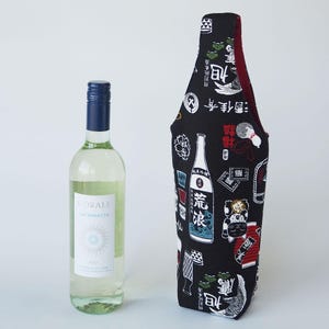 以下が含まれることがあります： 青いスクリューキャップが付いた透明なガラス製のワインボトルと、背の高い布製のボトルカバー。カバーは黒地で、白い文字の漢字、日本酒のボトルのイラスト、招き猫が描かれた白、赤、緑の模様が施されています。