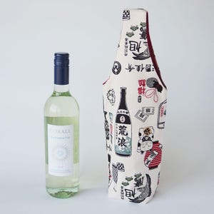 以下が含まれることがあります： 青いキャップとCorale Catarrattoと書かれた白いラベルが付いた透明なガラス製のワインボトルと、黒、赤、緑の日本風のイラストが繰り返し描かれた、背の高いオフホワイトの布製ボトルバッグ。