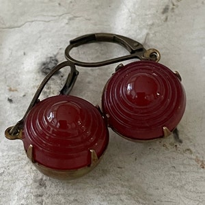 May include: A pair of red glass earrings with a brass setting. The earrings are round and have a textured surface.