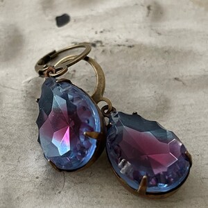 May include: A pair of teardrop-shaped earrings with iridescent blue and purple glass stones set in antique brass settings.