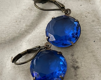 Puede incluir: Un par de pendientes de cristal azul con cierres de palanca de bronce antiguo. Los pendientes presentan grandes piedras redondas de cristal azul facetadas.