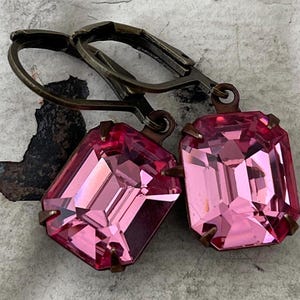 May include: A pair of pink gemstone earrings with antique brass leverback closures. The gemstones are emerald cut and have a faceted finish.