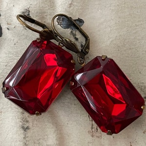 May include: A pair of red gemstone earrings with antique brass ear wires. The gemstones are faceted and have a rectangular shape.