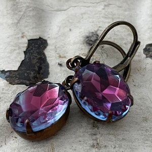 May include: A pair of dangle earrings with a purple and blue iridescent glass stone set in a copper tone metal setting.
