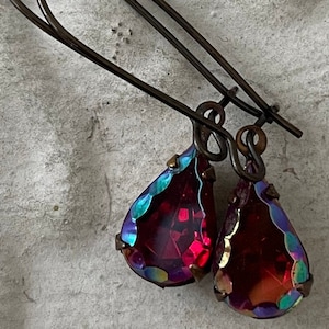 May include: A pair of dangle earrings with teardrop-shaped red iridescent glass stones and bronze-colored wire hooks.