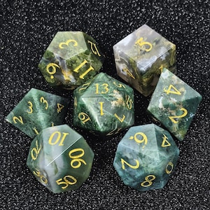 Könnte beinhalten: Set aus sieben polyedrischen Würfeln mit Moosachat-Optik. Die Würfel sind grün und weiß mit goldfarbenen Zahlen. Diese Würfel werden für Tabletop-Rollenspiele verwendet.