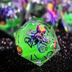 Könnte beinhalten: Ein klarer, vielseitiger Würfel mit grünem Inneren, der ein farbenfrohes Oktopus-Design aufweist. Der Oktopus hat lila, rosa und gelbe Farbtöne. Der Würfel hat silberne Zahlen und ist vor einem dunklen, strukturierten Hintergrund platziert.