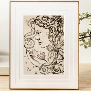 May include: Framed black and white art print featuring a woman's profile holding starfish. The artwork has intricate details, with flowing hair and decorative elements. The frame is gold-colored, and the print is displayed on a wooden surface.