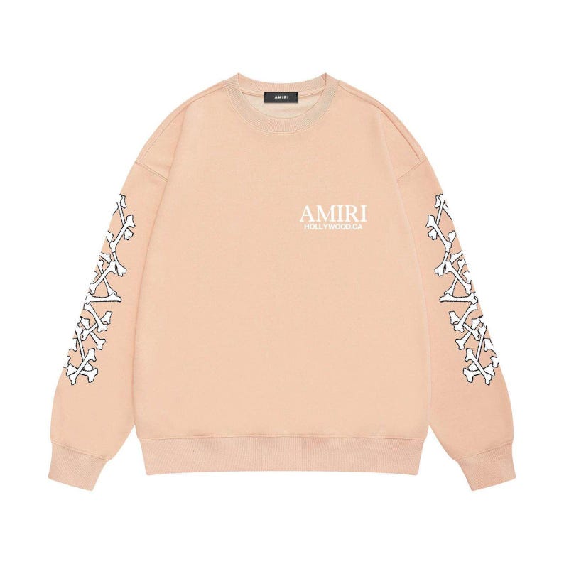 May include: A pale peach sweatshirt featuring white bone patterns on the sleeves. The text "AMIRI HOLLYWOOD.CA" is printed on the chest. The sweatshirt has a crew neck and long sleeves.