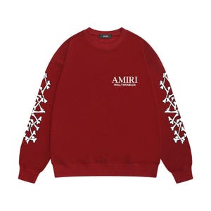 May include: A maroon sweatshirt featuring white bone patterns on the sleeves and the text "AMIRI HOLLYWOOD.CA" on the chest. The top has a crew neck and long sleeves.