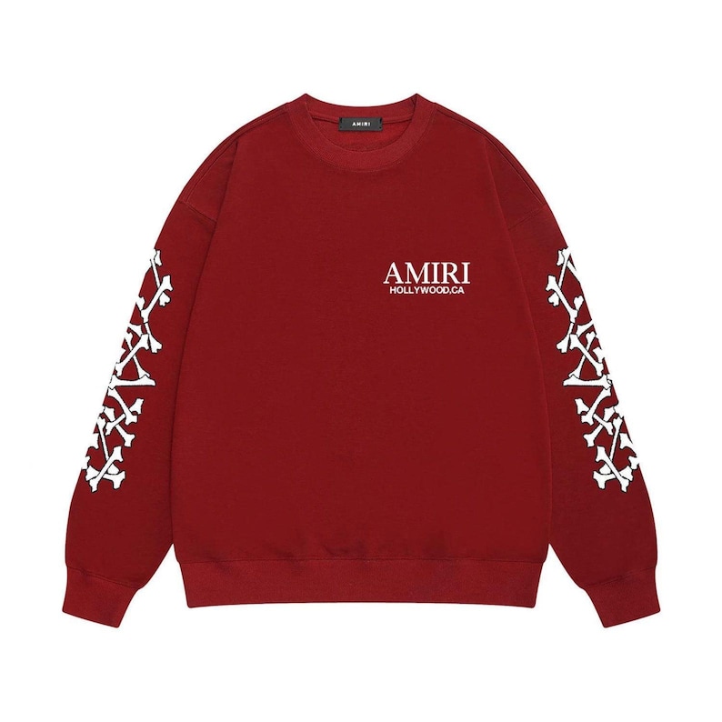 May include: A maroon sweatshirt featuring white bone patterns on the sleeves and the text "AMIRI HOLLYWOOD.CA" on the chest. The top has a crew neck and long sleeves.
