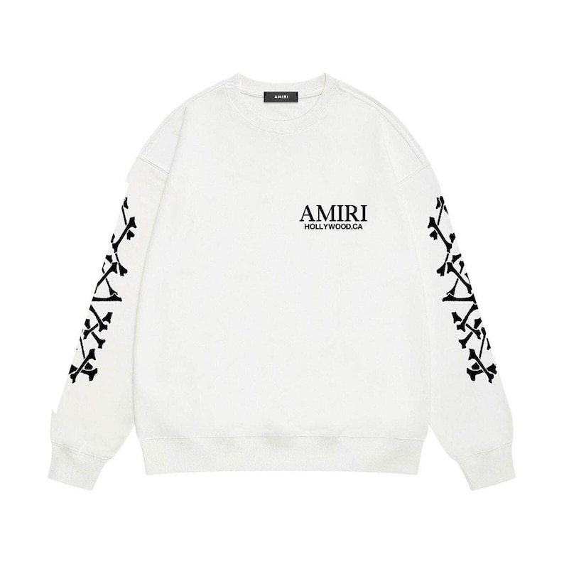 May include: White sweatshirt with black graphic details. The sleeves feature a black bone design. The chest displays the text "AMIRI HOLLYWOOD.CA" in black. A small black label is at the neckline.