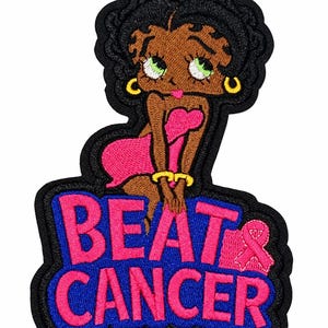 May include: An embroidered patch featuring a cartoon character with black hair, green eyes, and gold hoop earrings, wearing a pink dress. Below the character, the text BEAT CANCER is stitched in pink letters on a blue background with a pink ribbon.