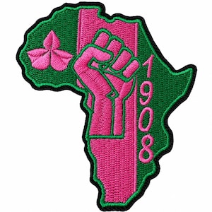 May include: An embroidered patch shaped like the continent of Africa in green with a black border. It features a pink raised fist, a pink three-leaf clover symbol, and the pink text 1908 arranged vertically along the right side of the design.