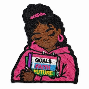 May include: An embroidered patch featuring a person with dark skin and black hair in a bun, wearing a bright pink hoodie and pink hoop earrings. The person holds a stack of three books with the words GOALS, FAITH, and FUTURE embroidered on them.