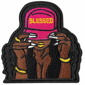May include: An embroidered patch featuring a dark-skinned figure wearing a bright pink baseball cap with the word BLESSED in yellow text. The figure has long white-tipped nails, gold bracelets, and gold lips, all outlined in black thread.