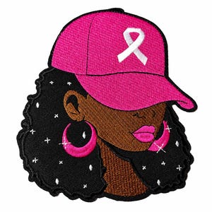 May include: An embroidered patch featuring a person with dark skin and voluminous black hair adorned with small white star accents. The person wears a bright pink baseball cap with a white ribbon symbol and large pink hoop earrings.