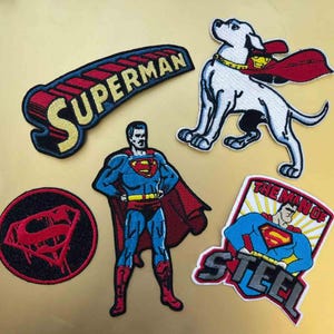 Könnte beinhalten: Eine Sammlung von aufgestickten Aufnähern mit Superman und verwandten Charakteren. Enthält einen Aufnäher mit dem Wort "SUPERMAN", einen Hund mit Umhang und verschiedene Superman-Posen. Die Aufnäher sind in Rot, Blau, Gelb und Schwarz gehalten.
