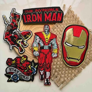 Puede incluir: Colección de parches bordados con personajes de Marvel Comics. Incluye a Deadpool, Iron Man, Coloso y una máscara de Iron Man. Los parches son de varios colores, incluyendo rojo, dorado, negro y azul, con costuras y texto detallados.