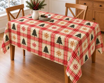 Könnte beinhalten: Eine rechteckige Tischdecke mit rot-weißem Karomuster, verziert mit wiederkehrenden grünen Weihnachtsbäumen und goldenen Schneeflocken. Der Stoff bedeckt einen Holztisch mit zwei Stühlen und einer weißen Kanne mit Tannengrün.