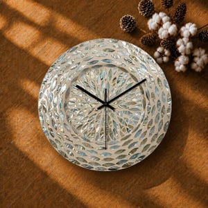 May include: A circular wall clock featuring a mosaic face composed of iridescent, petal-shaped mother-of-pearl tiles arranged in concentric patterns. The clock has three thin, black metal hands positioned at the center, indicating the time.
