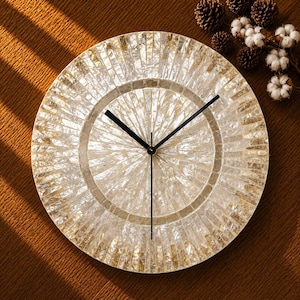 May include: A round wall clock featuring a mosaic face crafted from iridescent, cream-colored shell tiles arranged in a sunburst pattern. The clock has three thin, black metal hands positioned at the center, with no numerals on the dial surface.