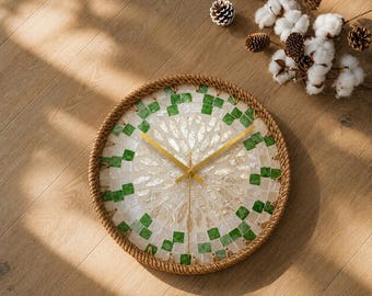 Könnte beinhalten: Eine runde Wanduhr mit einem Mosaikzifferblatt aus irisierenden weißen Muschelstücken und kleinen grünen quadratischen Fliesen. Die Uhr ist von einem dicken, gedrehten Rand aus Natur-Juteseil umgeben und hat dünne, goldfarbene Metallzeiger.