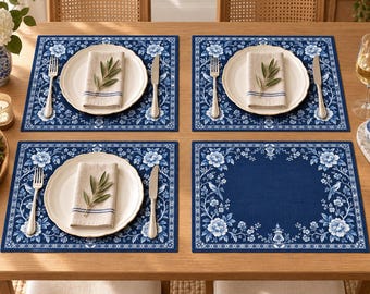 Könnte beinhalten: Vier rechteckige Platzsets mit dunkelblauem Hintergrund und einem weißen Blumen- und Vogelmuster am Rand. Drei Platzsets sind mit einem weißen Keramikteller, einer gefalteten beigen Serviette mit blauen Streifen, einer silbernen Gabel und einem silbernen Messer gedeckt.