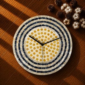 May include: A circular wall clock featuring a central cream-colored face decorated with a repeating pattern of small yellow flowers. The frame is composed of concentric rings of iridescent white shell tiles and dark navy blue rectangular tiles.