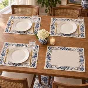 Pode incluir: Quatro jogos americanos retangulares com centro creme e borda floral azul e branca com motivos de pagode. Três lugares incluem um prato de cerâmica branca, um garfo dourado, uma faca dourada e um copo de vidro transparente.