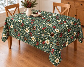 Könnte beinhalten: Eine rechteckige Tischdecke mit dunkelgrünem Hintergrund und einem sich wiederholenden Muster aus weißen Blüten, roten Beeren, Tannenzapfen und immergrünen Zweigen. Der Stoff liegt auf einem Holztisch mit zwei Holzstühlen.
