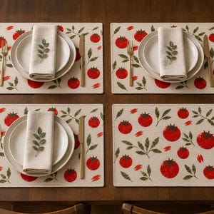 Pode incluir: Quatro jogos americanos retangulares com um padrão de tomates vermelhos e folhas verdes sobre um fundo bege claro. Cada lugar inclui um prato branco, um guardanapo bege dobrado com um raminho verde, um garfo e uma faca dourados.