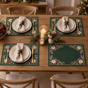 May include: A set of four rectangular dark green placemats featuring a floral border with white flowers, red berries, and green leaves. The placemats are arranged on a wooden table with white plates, beige napkins, gold cutlery, and a centrepiece.