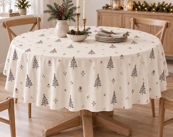 Könnte beinhalten: Eine runde, cremeweiße Tischdecke mit einem wiederkehrenden Muster aus dunkelgrünen Weihnachtsbäumen, kleinen roten Geschenken und goldenen Sternen. Der Stoff liegt auf einem runden Holztisch und bildet ein festliches Arrangement.