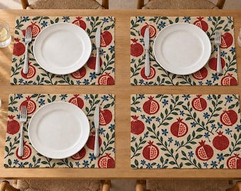 Könnte beinhalten: Ein Set aus vier rechteckigen Platzsets mit einem wiederkehrenden Muster aus roten Granatäpfeln, grünen Blättern und kleinen blauen Blumen auf beigem Grund. Jedes Platzset ist mit einem weißen Teller, einer Gabel und einem Messer gedeckt.