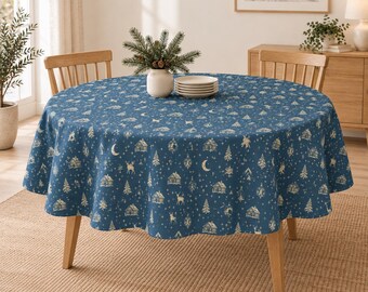Könnte beinhalten: Eine runde blaue Tischdecke mit einem sich wiederholenden weißen Muster aus Hütten, Tannenbäumen, Hirschen, Mondsicheln und Sternen. Der Stoff liegt auf einem runden Holztisch, auf dem ein Stapel weißer Teller und eine kleine Vase stehen.