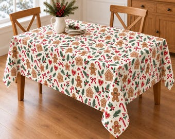 Könnte beinhalten: Eine rechteckige Tischdecke mit einem wiederkehrenden Muster aus Lebkuchenmännern, Lebkuchenhäusern, roten Herzen, Zuckerstangen und grünen Tannenzweigen auf cremefarbenem Grund, die einen Holztisch vollständig bedeckt.