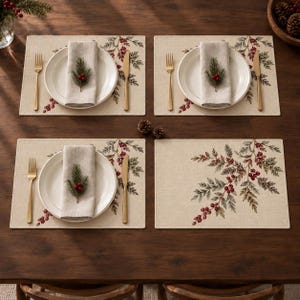May include: A set of four rectangular placemats featuring a printed pattern of green pine branches and red berries. Three settings include a white ceramic plate, a beige linen napkin topped with a sprig of pine and berries, a gold fork, and a gold knife.